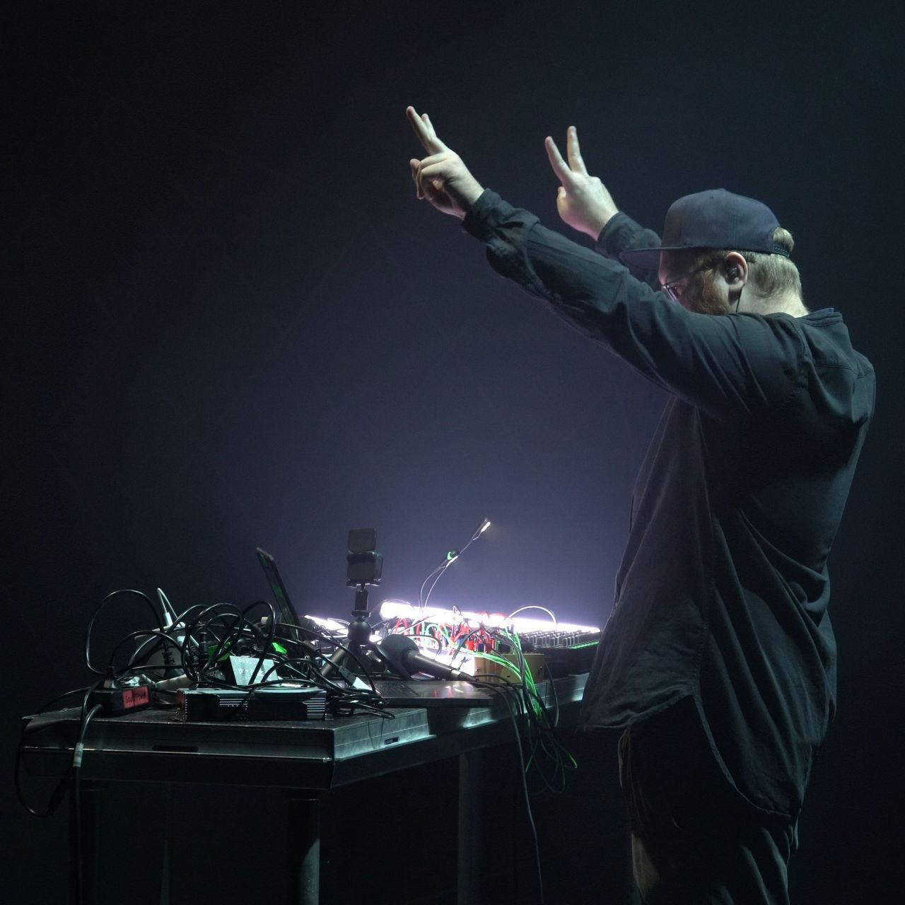 man giving the peace sign behind music gear